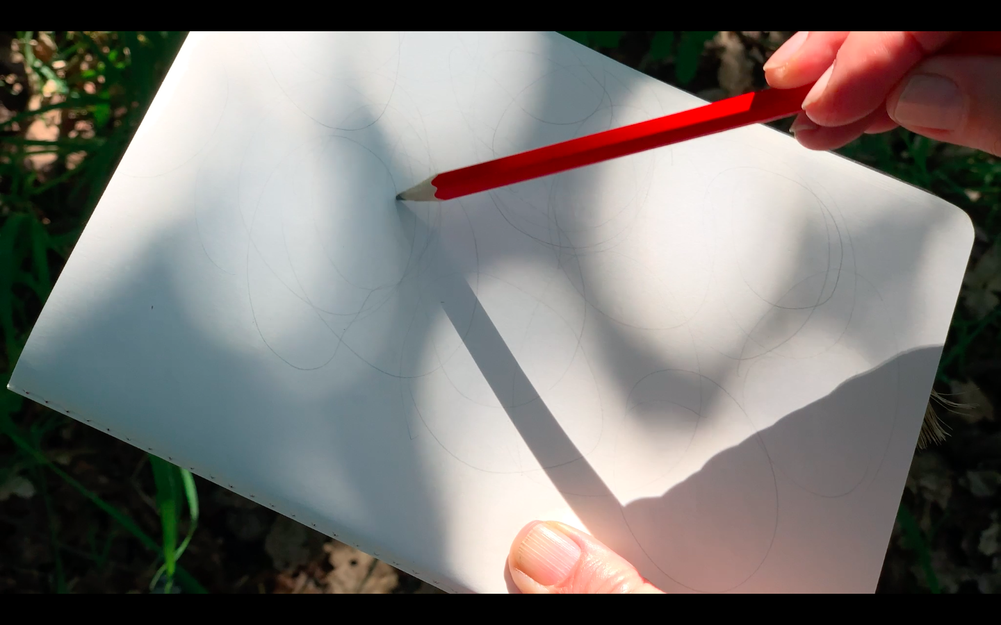 A white page and a red pencil: tracing light shadows that appear as circles
