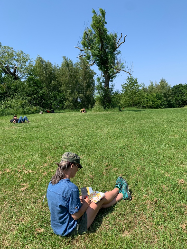 A woman wearing shorts sits on grass, drawing