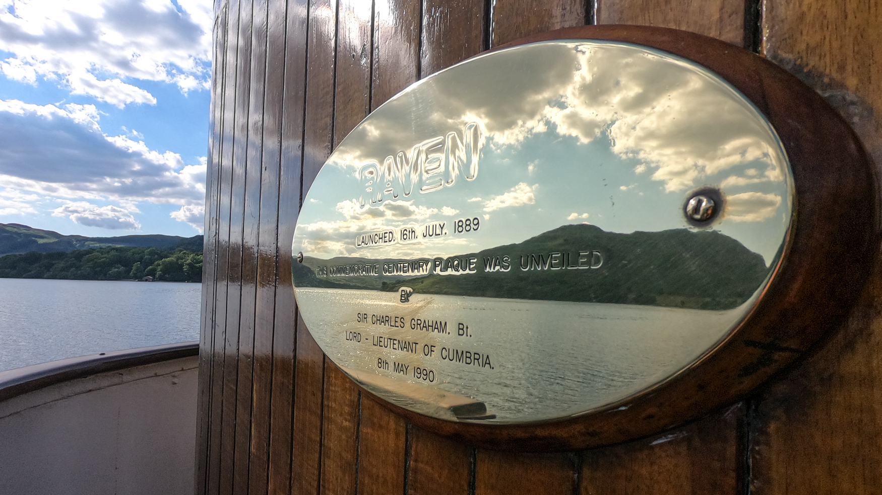 An oblong plaque on a boat reflects the lake and hills