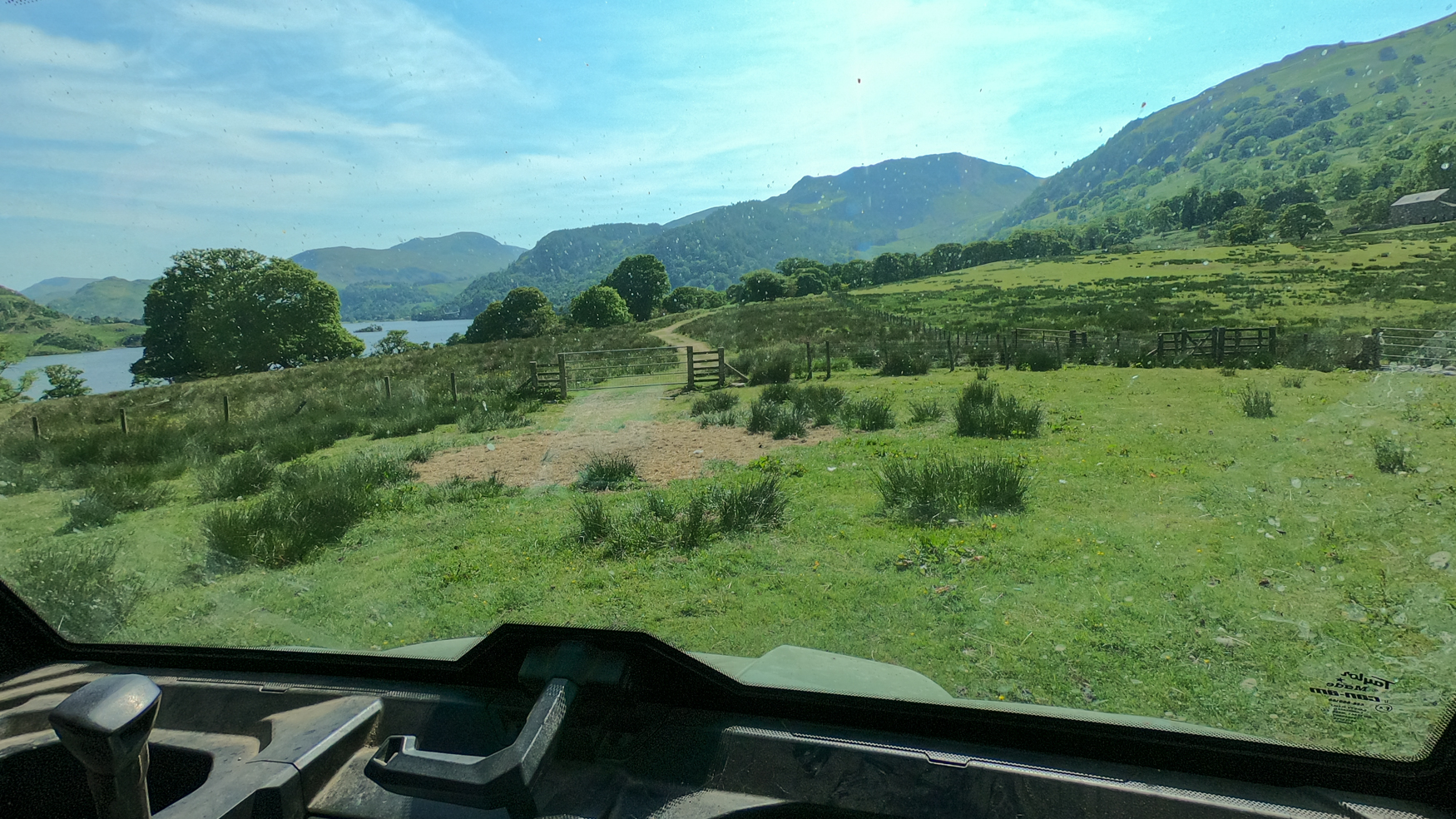 View through the windscreen of a quad bike, looking across green fields towards distant hills